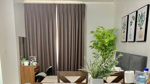 A dining area with a wooden table, cushioned chairs, a potted plant, and a grey sofa. - 1 Bedroom With Free Parking (Morong)