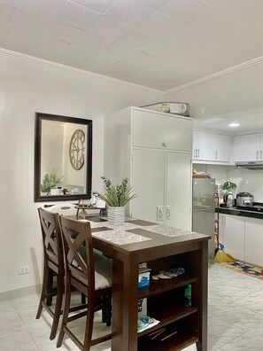 A dining area with a wooden table and chairs, a clock on the wall, and a white cabinet with a plant on top.