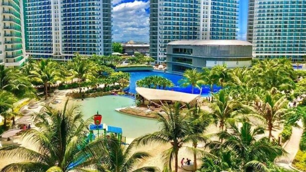 Ein Resort mit mehreren Hochhäusern, einem zentral gelegenen Poolbereich und umliegenden Palmen.