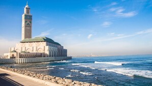 A coastal building with a prominent tower, a waterfront promenade, and a clear blue sky. - Nice Apartment For Families- Bd Ghandi- Casablanca (Casablanca)