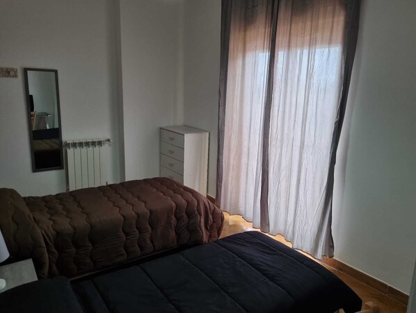 Un dormitorio con cama, cómoda, espejo y ventana con cortinas.