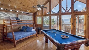 Une cabane en bois avec un lit superposé, une table de billard et de grandes fenêtres.