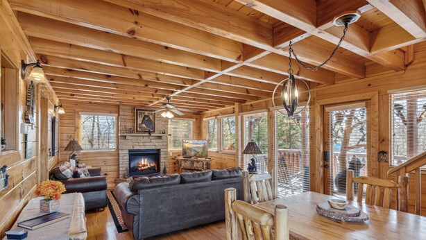 Un intérieur de chalet chaleureux avec une cheminée, des meubles en bois et de grandes fenêtres.