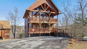 Une cabane en bois à deux étages, dotée d’un balcon et d’un escalier menant à l’étage supérieur, avec un ciel dégagé en arrière-plan.