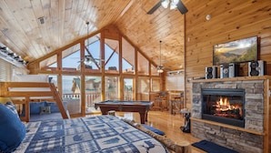 L’intérieur d’un chalet confortable, avec une grande chambre, une cheminée, une table de billard et une vue sur l’extérieur.