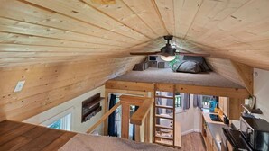 Un dormitorio tipo loft con techo inclinado, vigas de madera, una cama litera y una pequeña kitchenette.