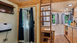 Un interior de madera con una puerta corredera, una escalera, una zona de cocina con armarios de madera y un calentador empotrado.