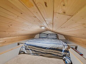 A small attic bedroom with a sloped ceiling, a bed with striped bedding, and a single light fixture.