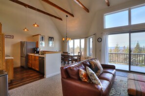 A spacious living area with a brown leather sofa, a dining table, and a kitchen with wooden cabinets and a refrigerator. - Saddleback - Rock Pond Condo 67 - ski in/out (Rangeley)