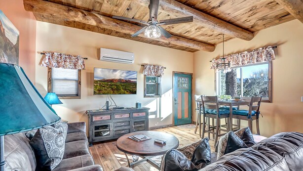 A cozy living room with a wooden ceiling, a television, a dining table with chairs, and a sofa with leather cushions. - Charming 660 sq. ft. Sedona Meadowlark Studio with stunning red rock views! (Sedona)