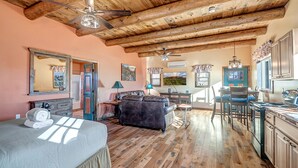 A spacious room with wooden floors, a ceiling fan, a bed, a sofa, a dining table with chairs, and a kitchen area. - Charming 660 sq. ft. Sedona Meadowlark Studio with stunning red rock views! (Sedona)