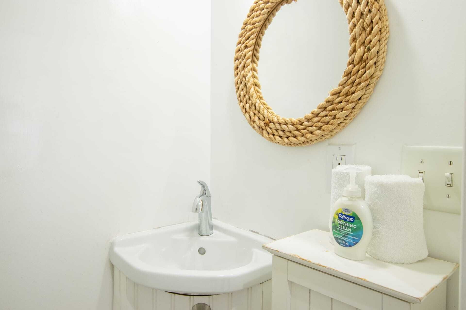 Un baño con un lavamanos blanco, un adorno de cuerda trenzada y una botella de Softsoap Soothing Clean sobre el mostrador.
