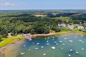 An aerial view of a coastal area with a marina filled with boats, surrounded by dense greenery and residential buildings.