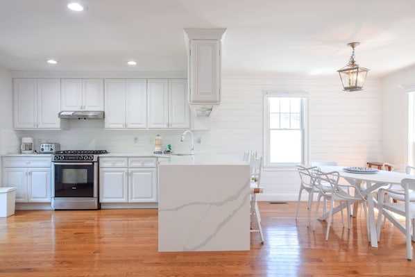 A modern kitchen with white cabinetry, a central island, and a dining area with white chairs.