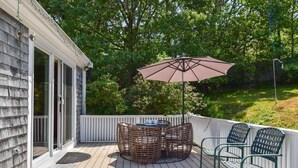 Une terrasse avec une table et des chaises, un grand parasol et une clôture blanche.