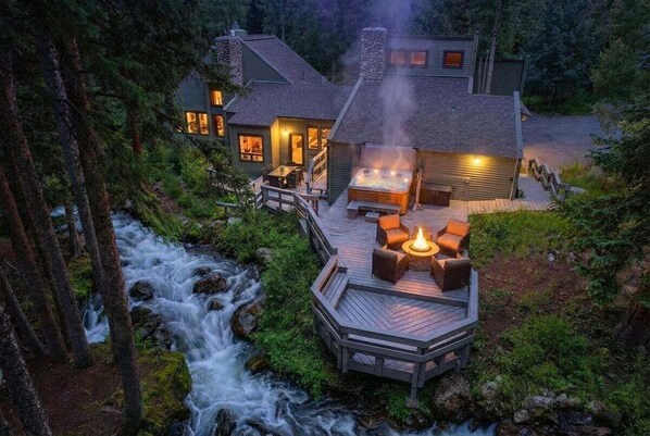A cabin with a hot tub, deck, and a stream.