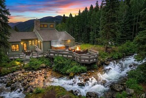 A lodge with a hot tub, outdoor seating, and a view of a flowing river.