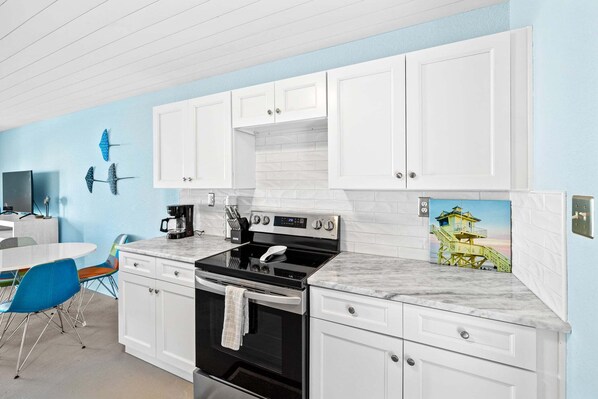 A modern kitchen with white cabinets, a black stove, and a blue wall with a mural.