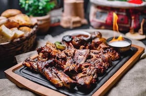 Tarjottimella on grillattuja kylkiluita, sytytetty kynttilä ja pieni kulho kastiketta.