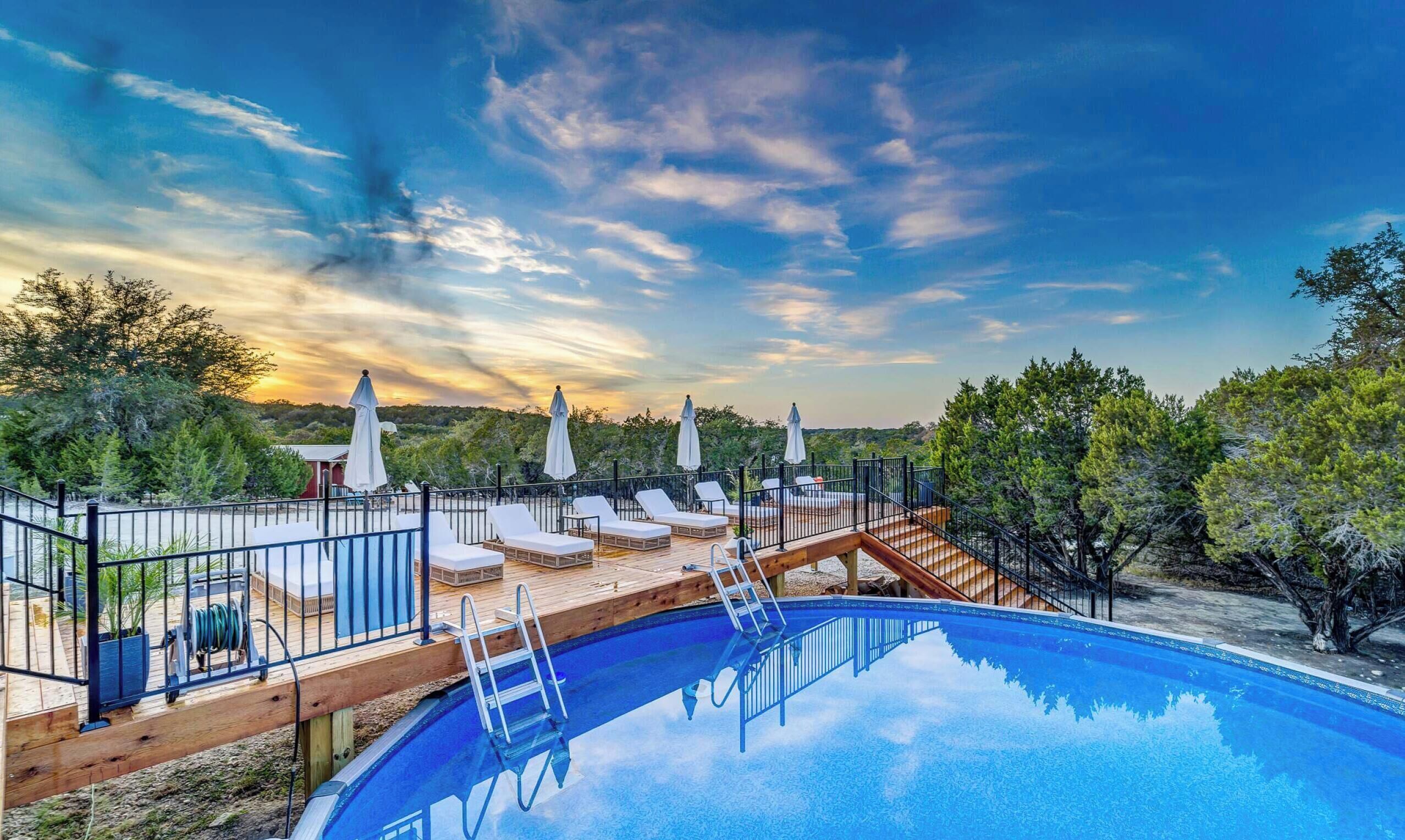 Una piscina amb gandules i ombrelles, envoltada d'arbres i un pont de fusta.