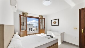 Un dormitorio con cama, ventana con cortinas, radiador y puerta.