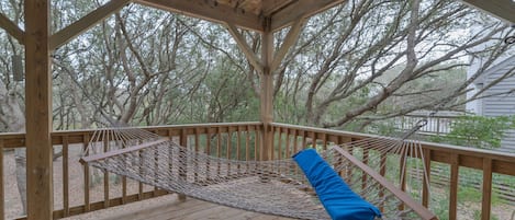 A wooden deck with a hammock and a blue cushion.