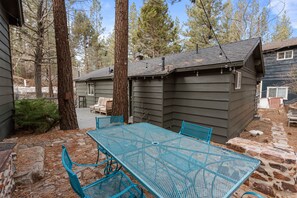 A patio with a metal table and chairs, surrounded by stone walls and trees.