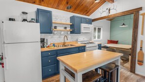 Une cuisine avec des meubles de couleur bleue, un réfrigérateur blanc, une table en bois et une cuisinière.