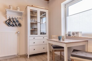 Une cuisine avec des meubles blancs, une table et une fenêtre équipée de stores.