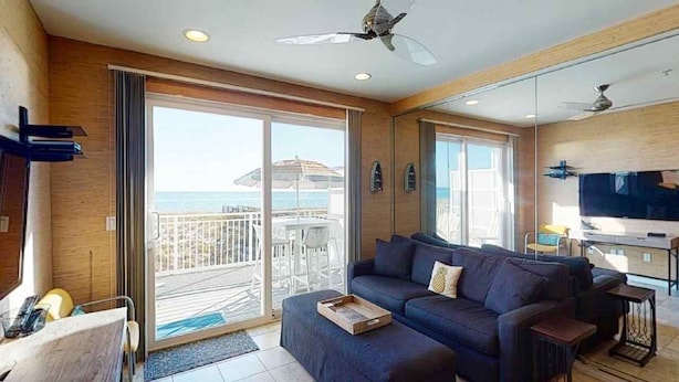 A modern living room with a sofa, a TV, and a balcony with a view of the sea. - Southern Jewel 1 Bedroom | 1.5 Baths | Sleeps 4 (Navarre Beach)