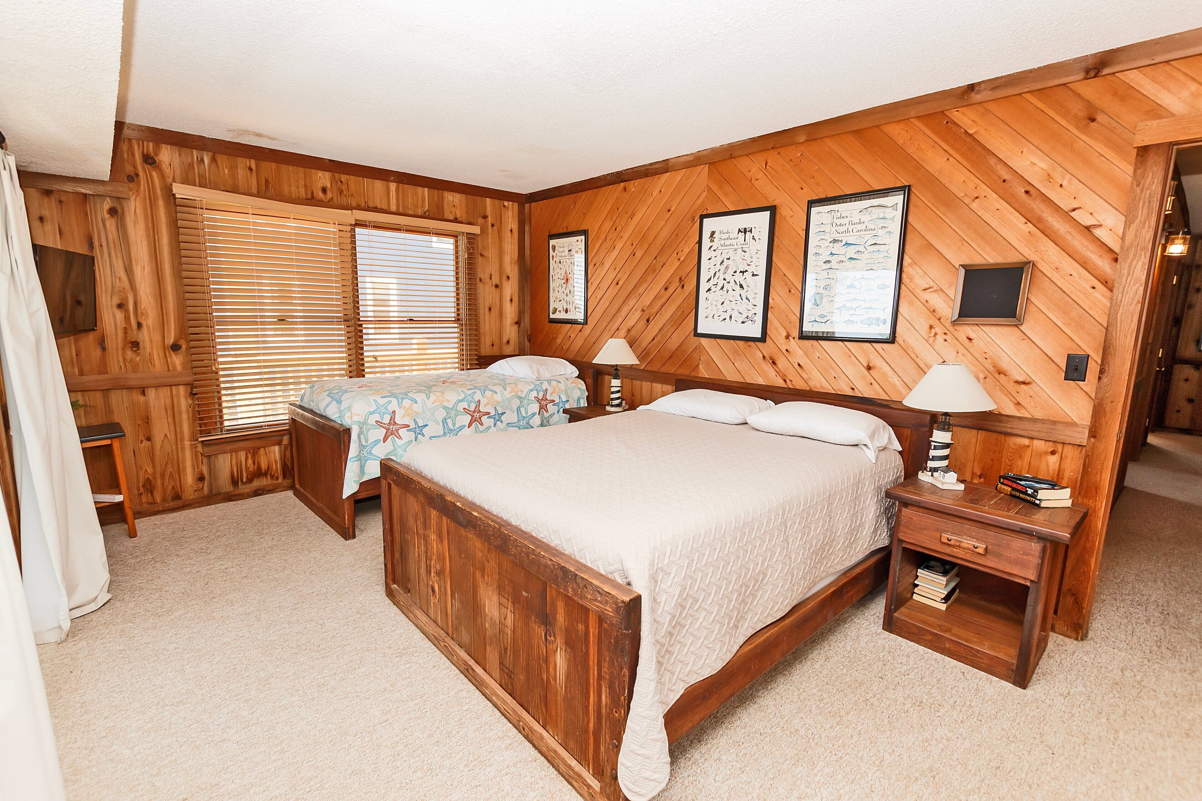 A wooden-paneled bedroom with two beds, a nightstand, and framed pictures on the wall.