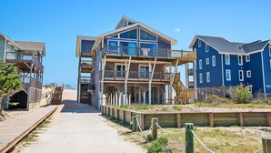 A beachfront property with a wooden boardwalk leading to a multi-level building with balconies. - Oceanfront, Guest House, Hot Tub & Spacious Decks (Avon)