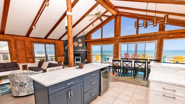 A spacious kitchen with large windows, a dining area with outdoor chairs, and a view of the ocean. - Oceanfront, Guest House, Hot Tub & Spacious Decks (Avon)
