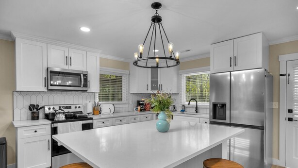 A modern kitchen with white cabinetry, a stainless steel refrigerator, a central island with stools, and a chandelier. - Southend Home walk 2 *Uptown Panthers Stadium Restaurants (Charlotte)