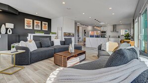 Un salon moderne avec un canapé gris, une table basse et, au fond, un coin repas.
