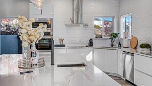 Une cuisine moderne avec des meubles blancs, des appareils en acier inoxydable et un plan de travail en marbre.