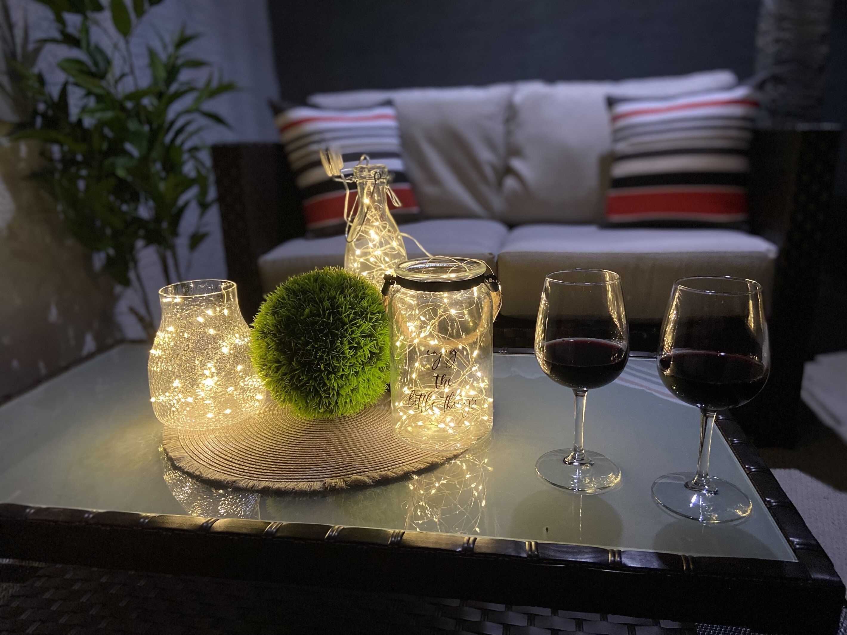 Una mesa con objetos decorativos, incluyendo un tarro de vidrio, una bola de musgo verde y dos copas de vino.