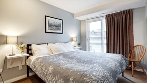 Un dormitorio con una cama grande, dos mesitas de noche con lámparas, un cuadro en la pared y una ventana con cortinas.