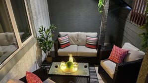 Un espacio al aire libre acogedor con un sofá y dos sillones, una mesa de centro con objetos decorativos y una planta en maceta.