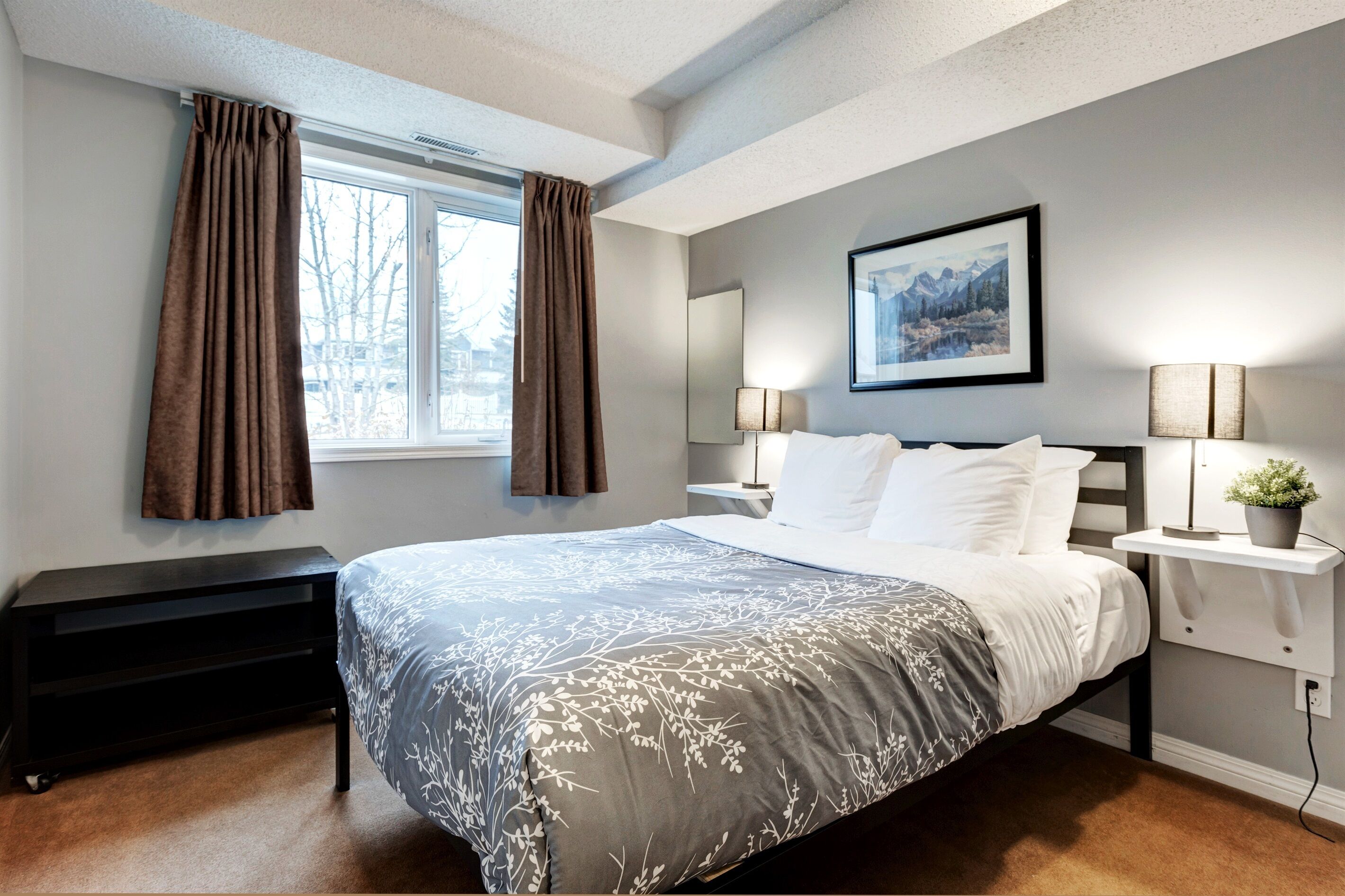 Een moderne slaapkamer met een groot bed, een nachtkastje, een raam met gordijnen en een ingelijst schilderij aan de muur.