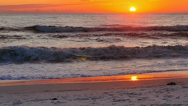 Una playa con olas, un atardecer y un cielo despejado.