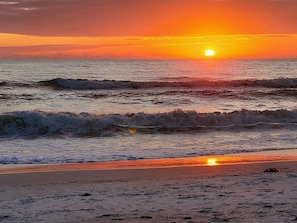 A beach with waves, a sunset, and a clear sky.