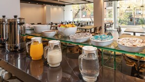 A breakfast buffet with various food items and beverages, including bowls of cereal, a coffee machine, and a pitcher of orange juice. - Hotel M (Mendoza)
