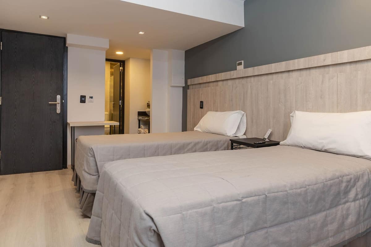 A hotel room with two beds, a small table, and a bathroom visible through an open door.