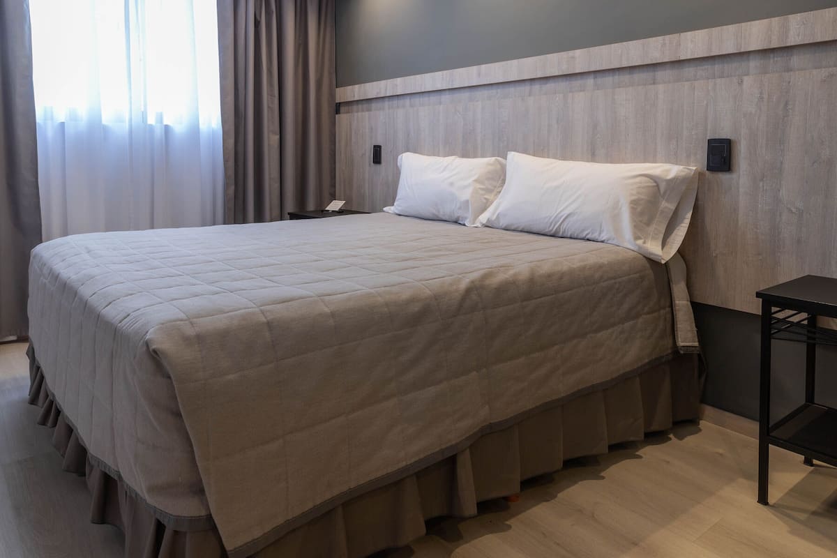 A neatly made bed with a quilted cover, a bedside table, and a nightstand with a phone.
