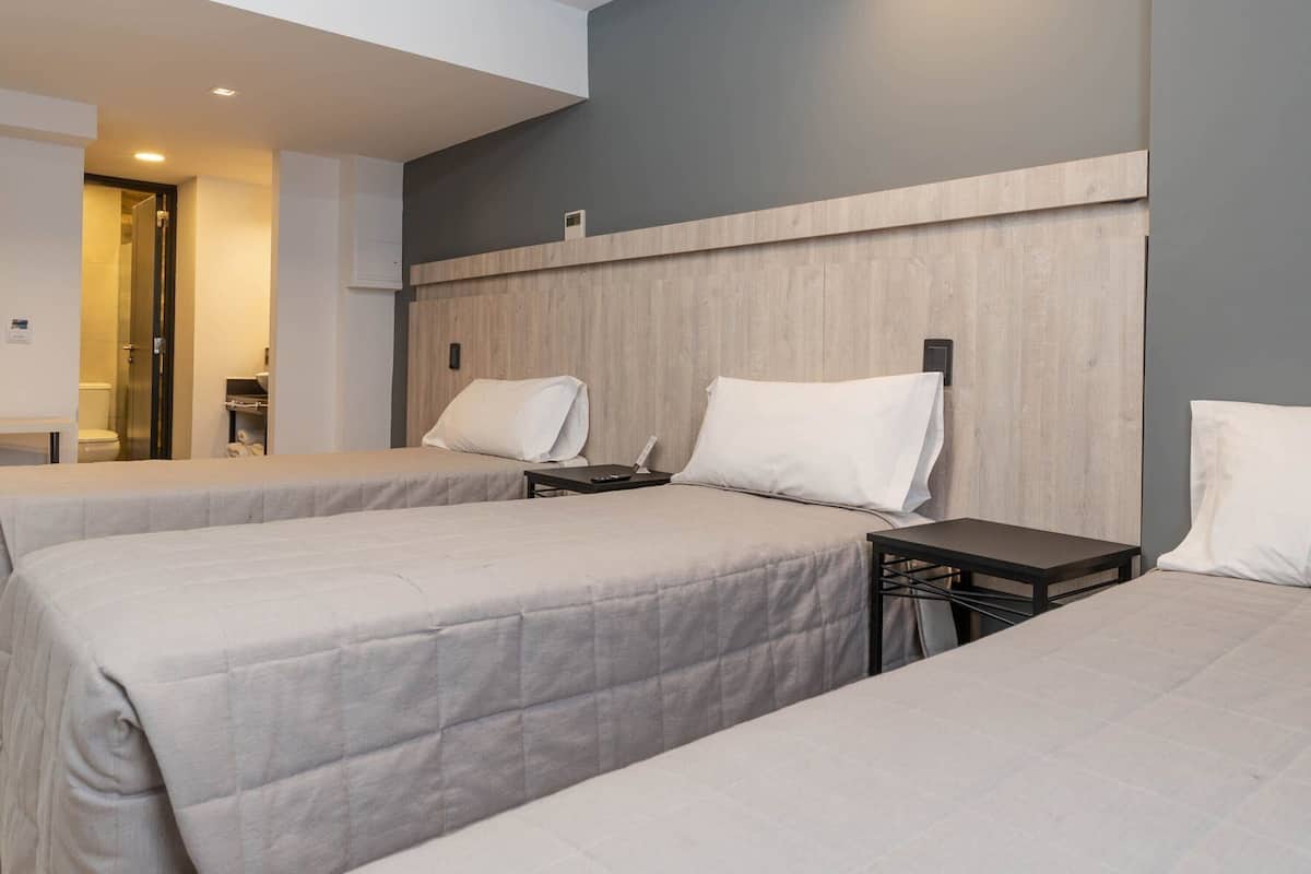 A hotel room with two beds, a nightstand, a desk, and a bathroom visible in the background.