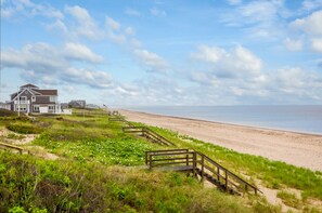 A beachfront property with a wooden staircase leading to a house, a sandy beach, and a clear sky. - Oceanfront Escape—Cape Cod Bay & Sandbars (East Sandwich)