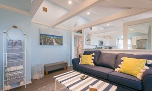A modern living room with a sofa, a striped coffee table, and a bench. A large mirror reflects the kitchen area. - Oceanfront Escape—Cape Cod Bay & Sandbars (East Sandwich)
