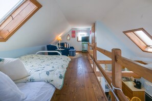 A cozy attic bedroom with a bed, a desk, and a chair. There is a window with a view of the outside.