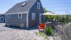 Une petite maison avec un toit en pente, un patio couvert avec une table et des chaises, et une allée gravillonnée.